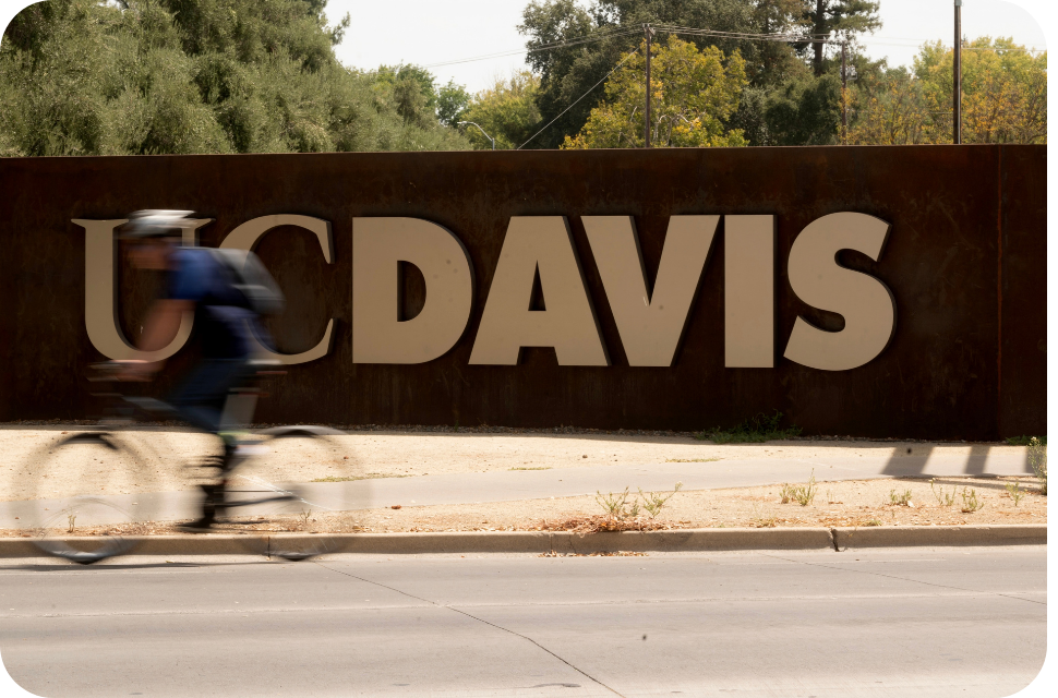 Large UC Davis metal sign with cyclist blurred in foreground
