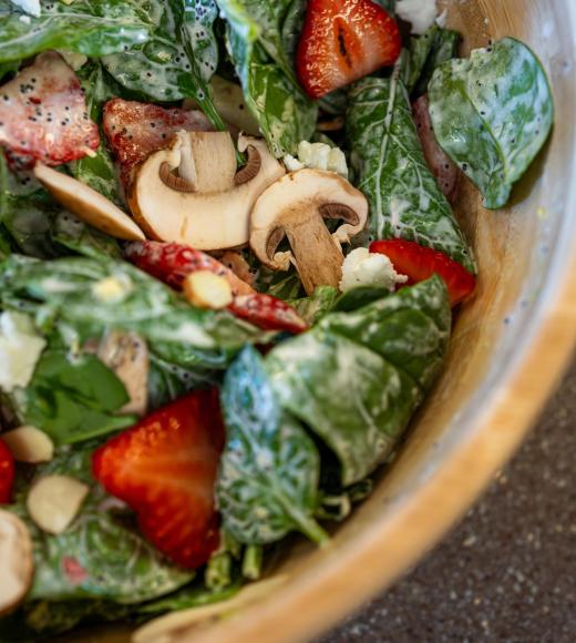 Close up of a bowl of salad with spinach, strawberries, cheese, mushrooms and avocado.