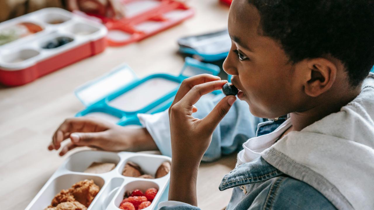 Young boy eating school lunch from a divided tray, focused at a cafeteria table